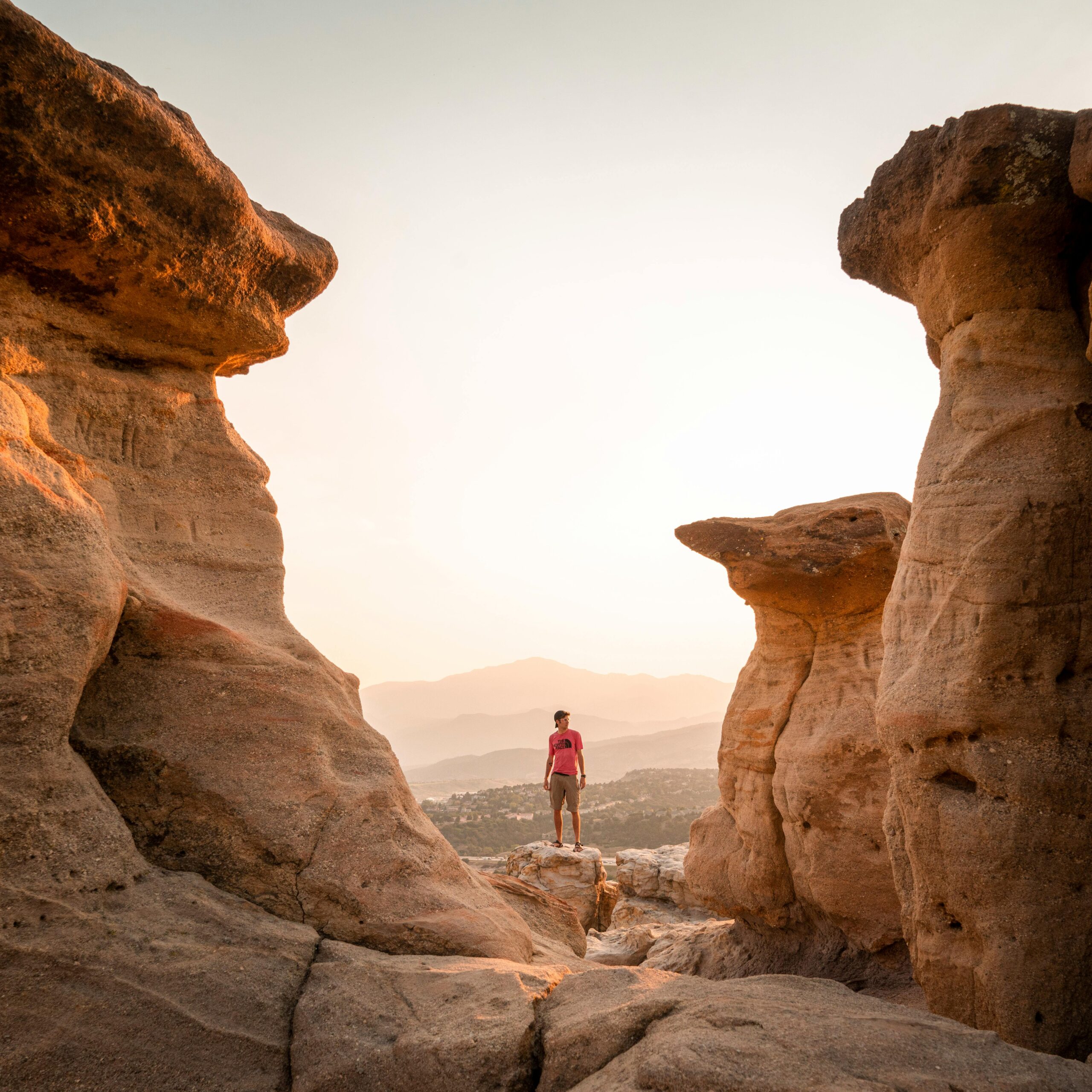 Hiker stands between scenic rock formations at sunset in Colorado Springs.